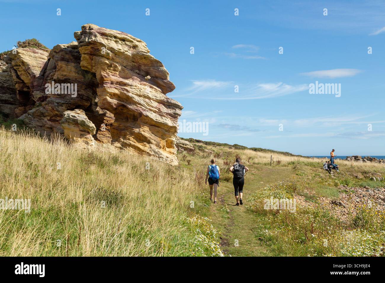 Spaziergänger passieren die Caiplie Caves - Höhlensystem, das lokal als die Buchten bekannt ist, auf dem Fife Coastal Path zwischen Anstruther und Crail, Fife, Schottland Stockfoto