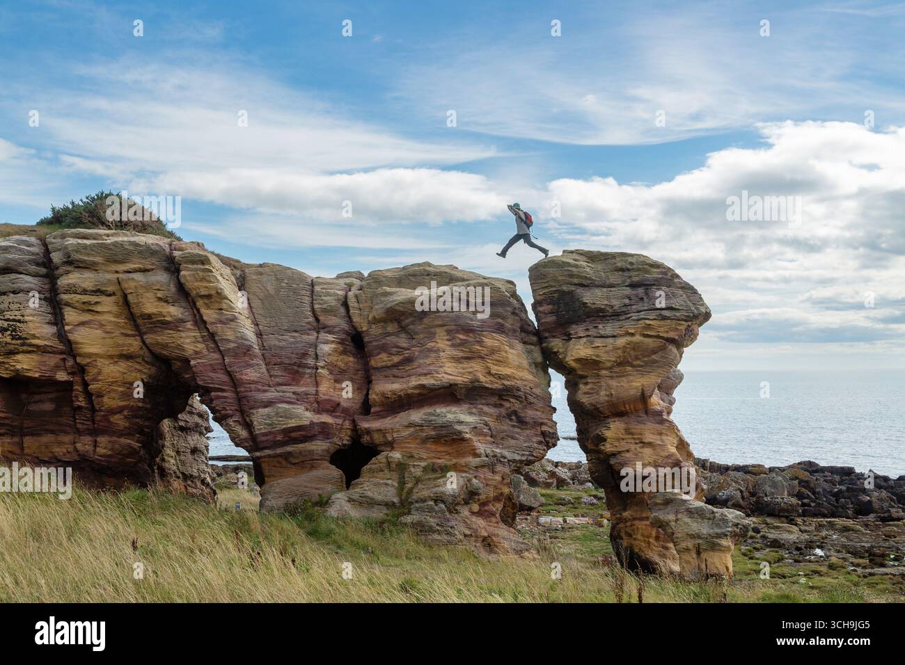 Eine Person, die auf den Caiplie Caves springt - Höhlensystem, das lokal als die Buchten bekannt ist, auf dem Fife Küstenpfad zwischen Anstruther und Crail, Fife, Schottland Stockfoto
