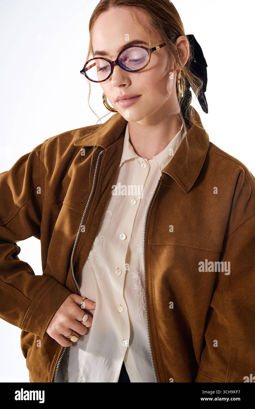 Eine selbstbewusste junge Frau glänzt in einem stilvollen Outfit mit einer braunen Jacke und einer schicken Brille. Stockfoto
