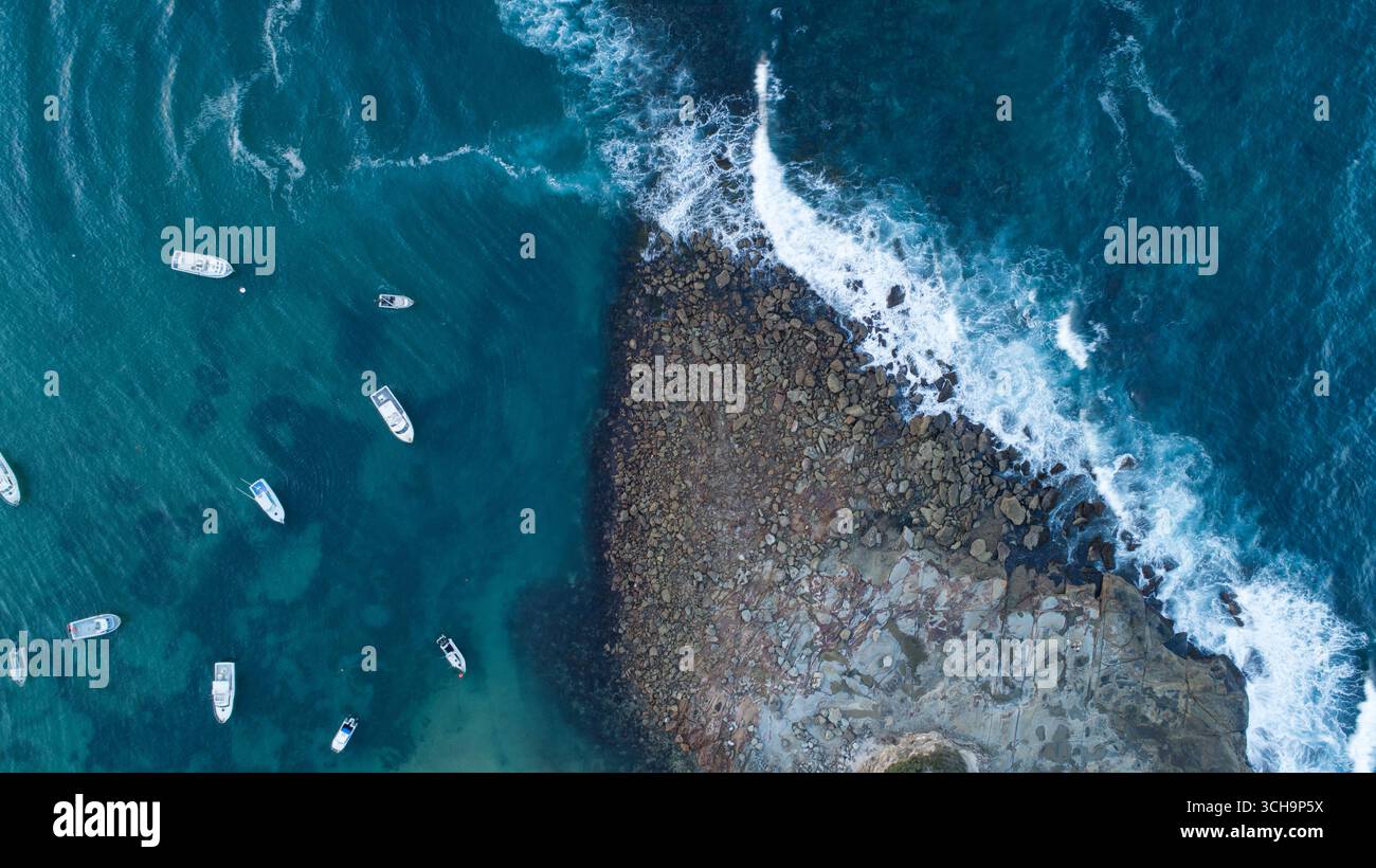 Aus der Vogelperspektive schweben Boote im ruhigen türkisfarbenen Wasser im Kontrast zu der zerklüfteten Küste in Sydney, New South Wales, Australien. Stockfoto