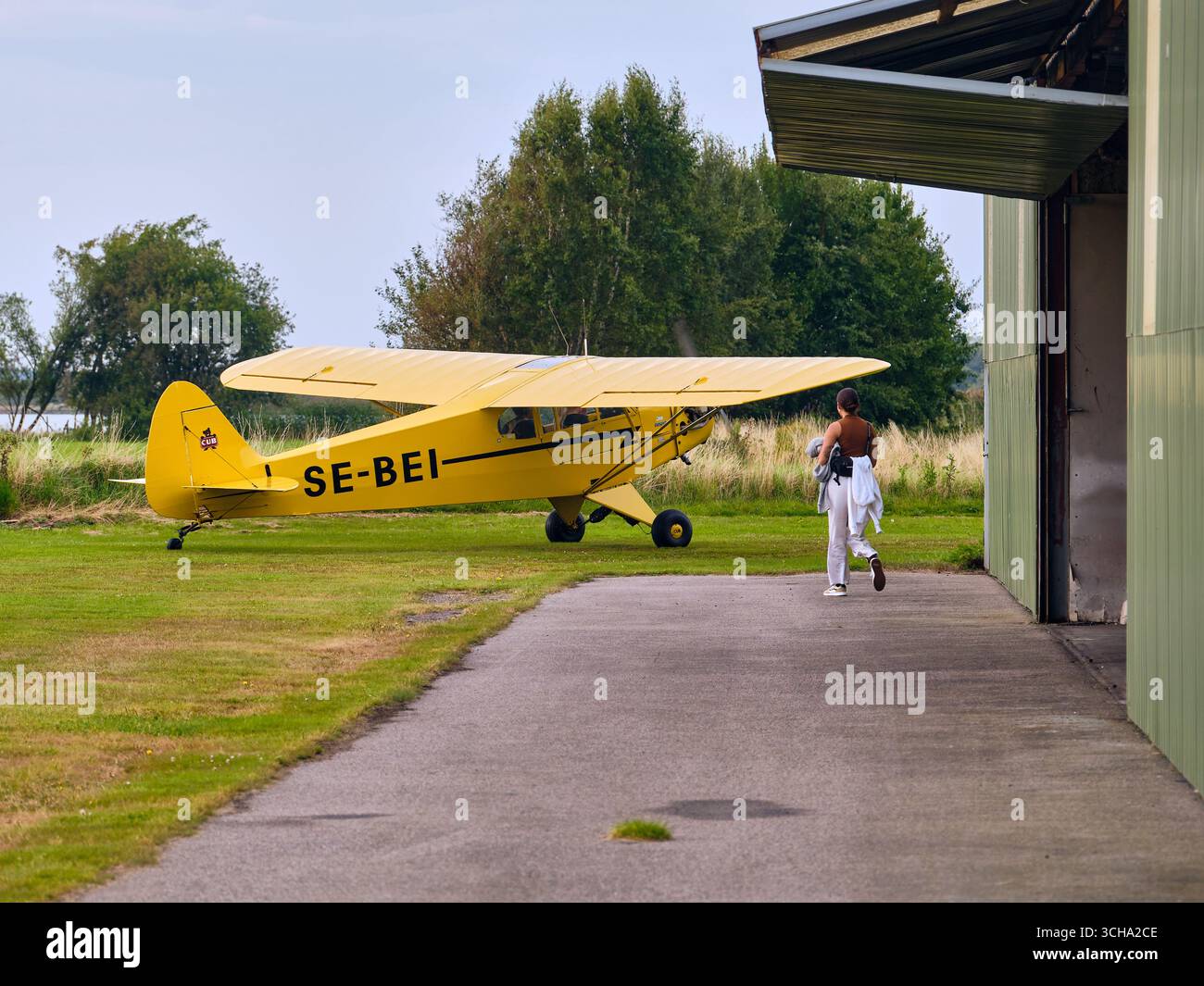 Varberg, Schweden; 28. August 2025: Piper Cub aus dem Jahre 1946, der auf dem Flugplatz Varberg als Familienmitglied in der Nähe des offenen Hangars steht. Stockfoto