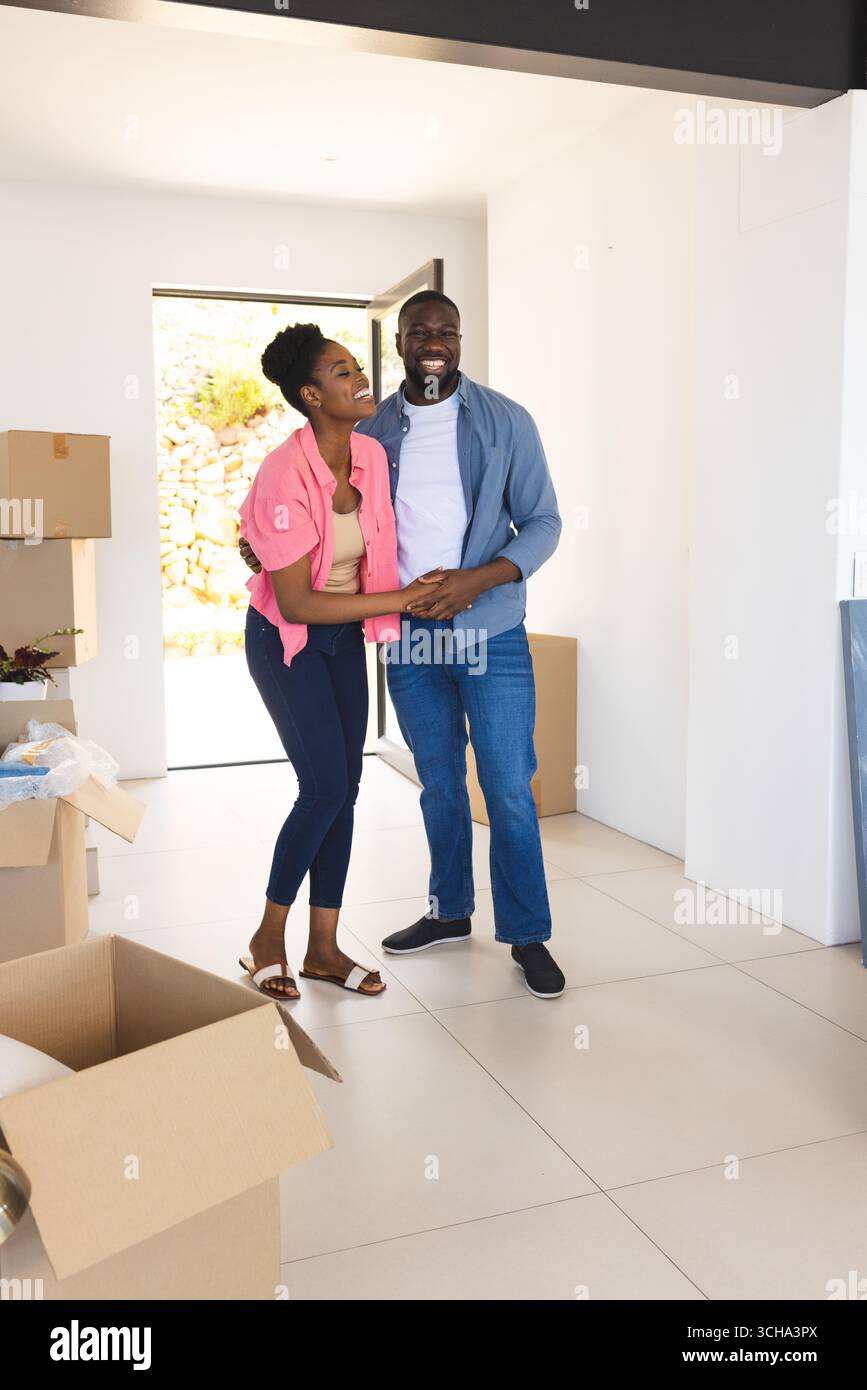 Glückliches afroamerikanisches Paar, das sich in ein neues Zuhause umgibt, umgeben von Umzugskartons, und gemeinsam feiert. Hausbesitz, Umzug, Auspacken, Liebe, Rela Stockfoto