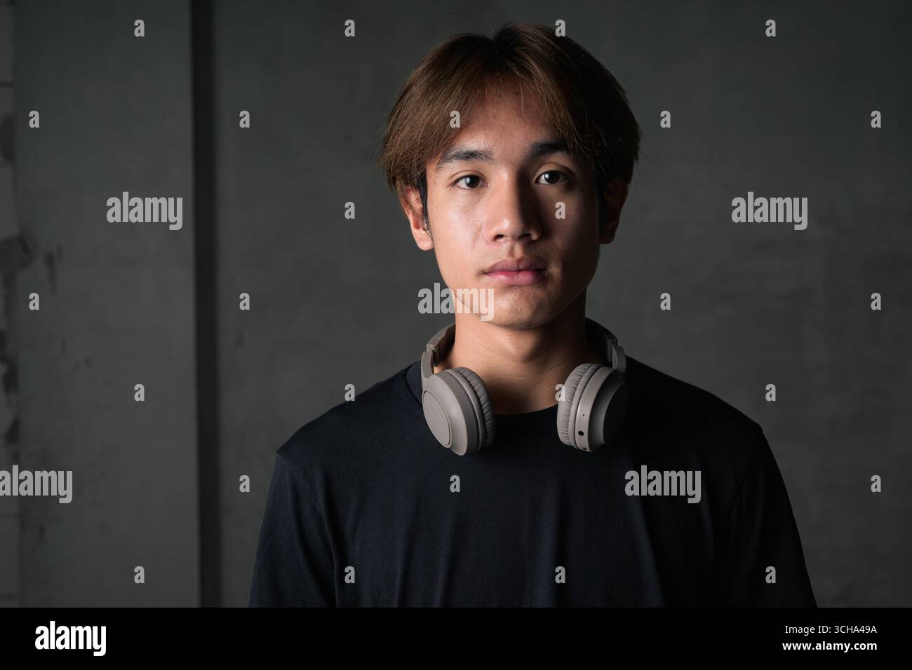 Junger thailändischer asiatischer Mann mit einem schwarzen T-Shirt, posiert in einem minimalistischen, brutalistischen Baubereich mit grauen Betonwänden Stockfoto