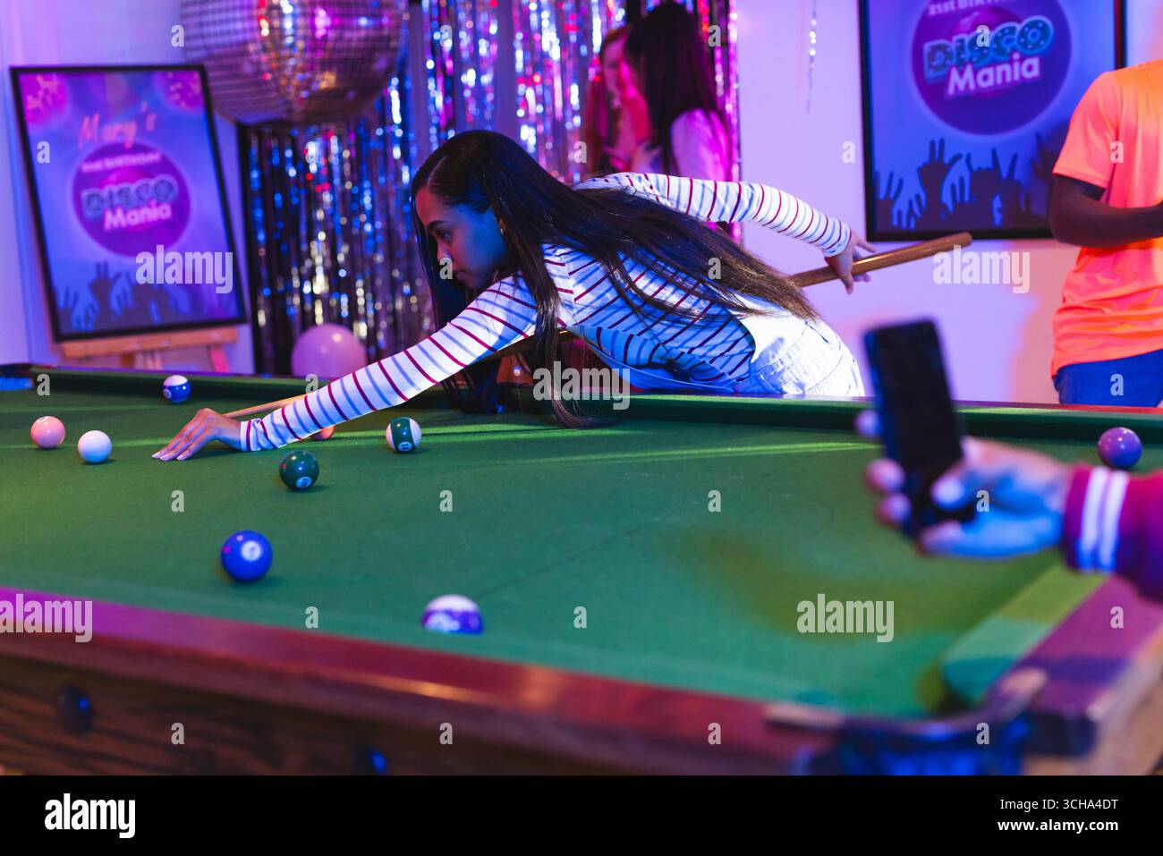 Teenager spielen Billard auf der Party, fokussieren sich auf den Schuss, während Freunde in der Nähe feiern, zu Hause. Billard, Feier, Teenager-Freunde, Freundschaft, Stockfoto