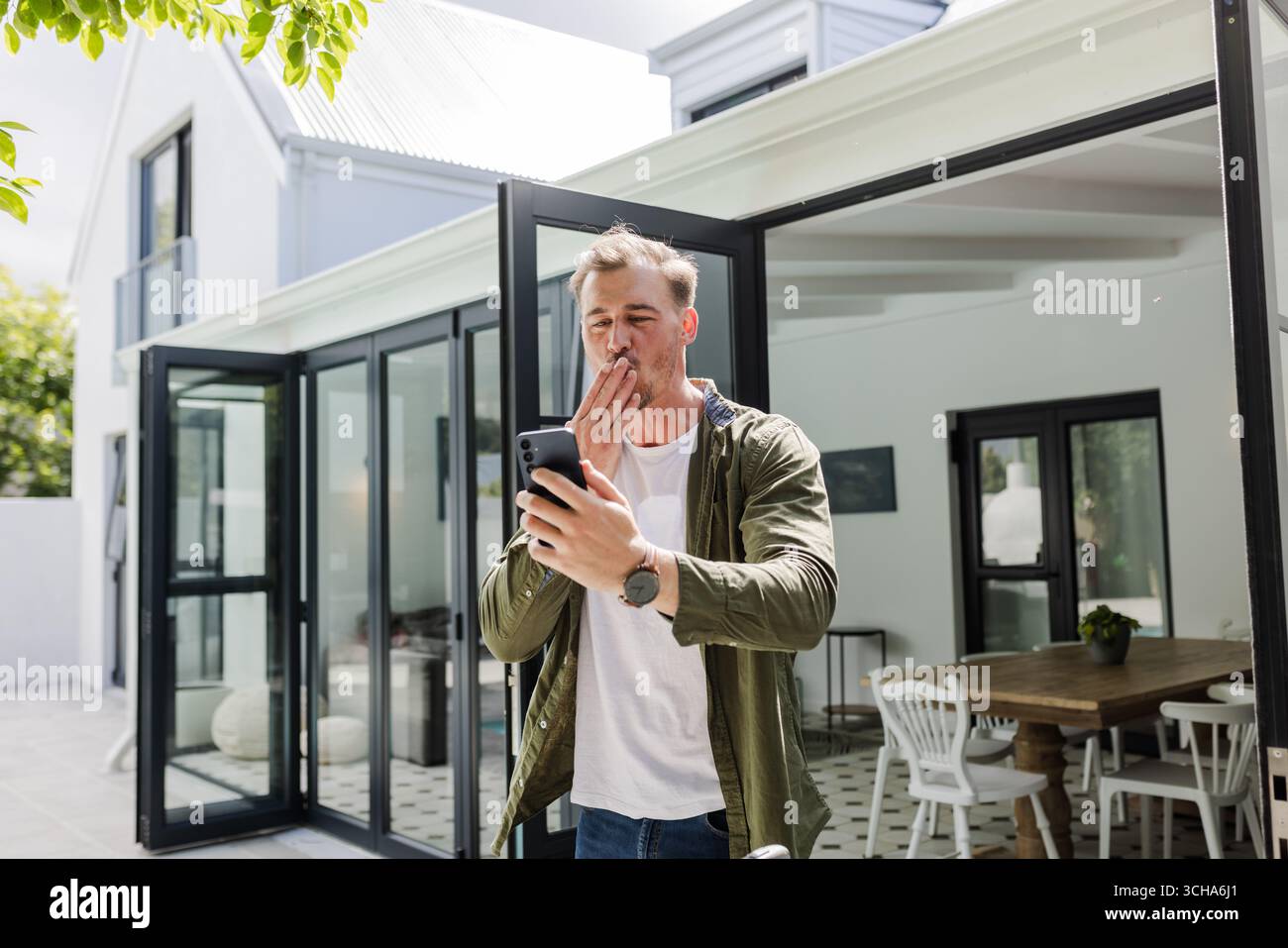 Mann draußen mit Smartphone, überrascht und lächelnd auf der modernen Terrasse. Technologie, Kommunikation, Lifestyle, Glück, Freizeit, Entspannung Stockfoto