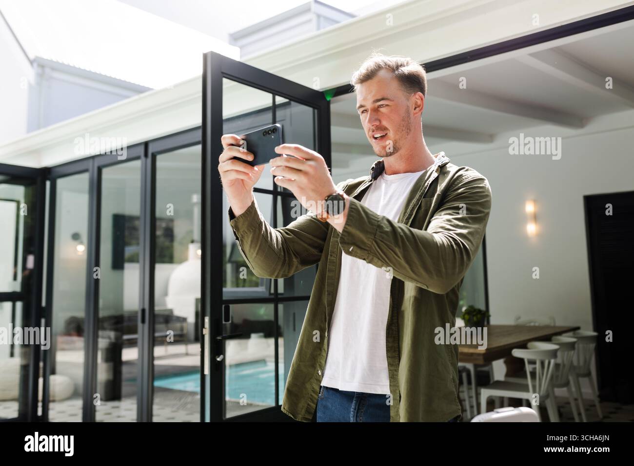 Junger Mann mit Smartphone, um Momente zu Hause festzuhalten, lächelnd und entspannt. Technologie, Freizeit, Lifestyle, Kommunikation, Entspannung, fröhlich Stockfoto