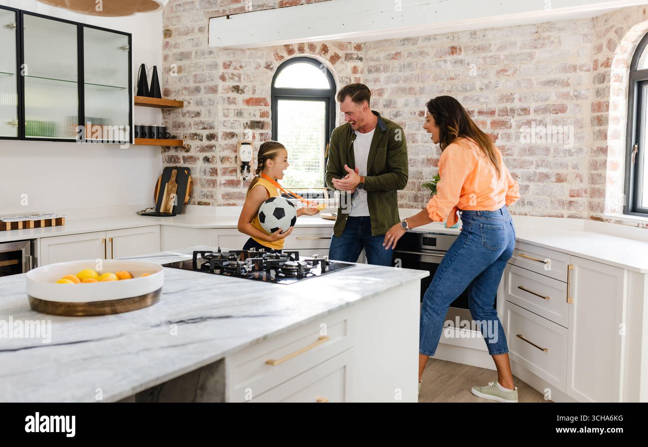 Familie spielt mit Fußball in der modernen Küche und genießt gute gemeinsame Zeit. Bindung, Aktivität, Zweisamkeit, Haushalt, Erziehung, Freizeit Stockfoto