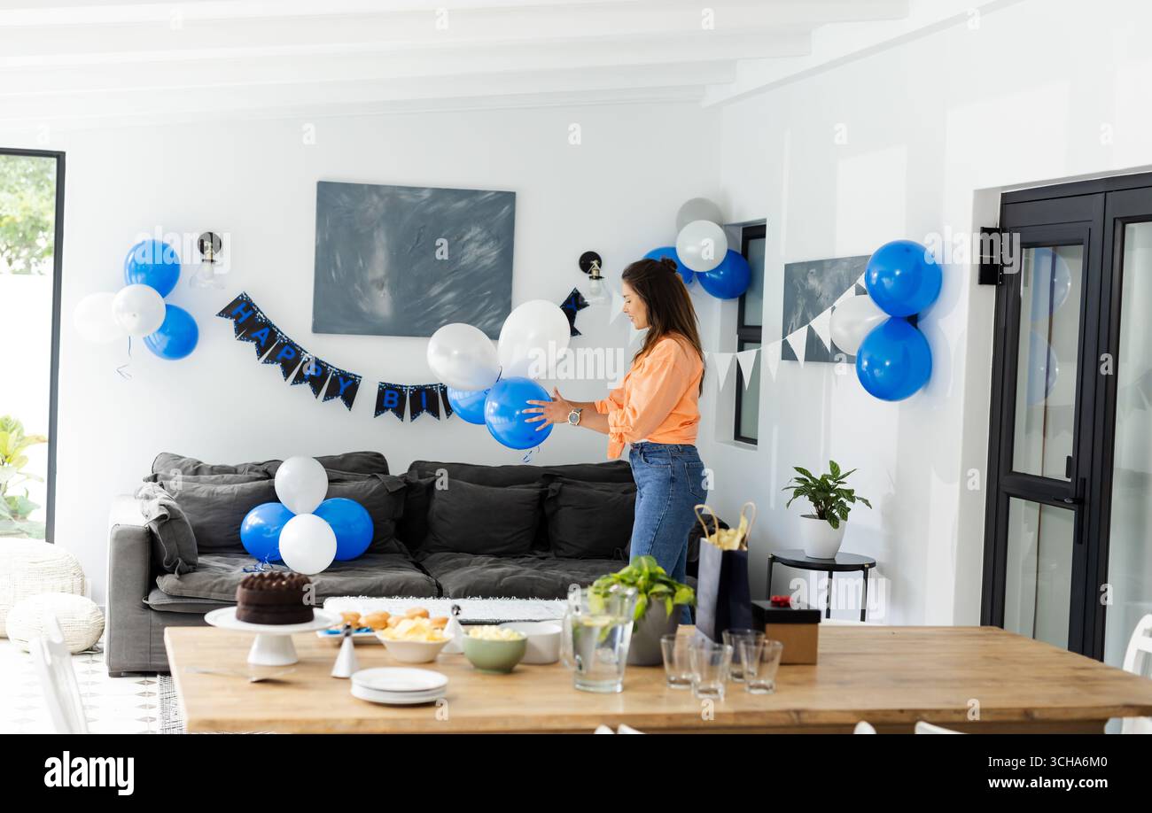 Frau dekoriert Wohnzimmer mit Ballons für Geburtstagsfeier zu Hause. Party, festlich, Dekoration, Inneneinrichtung, Vorbereitung, fröhlich Stockfoto