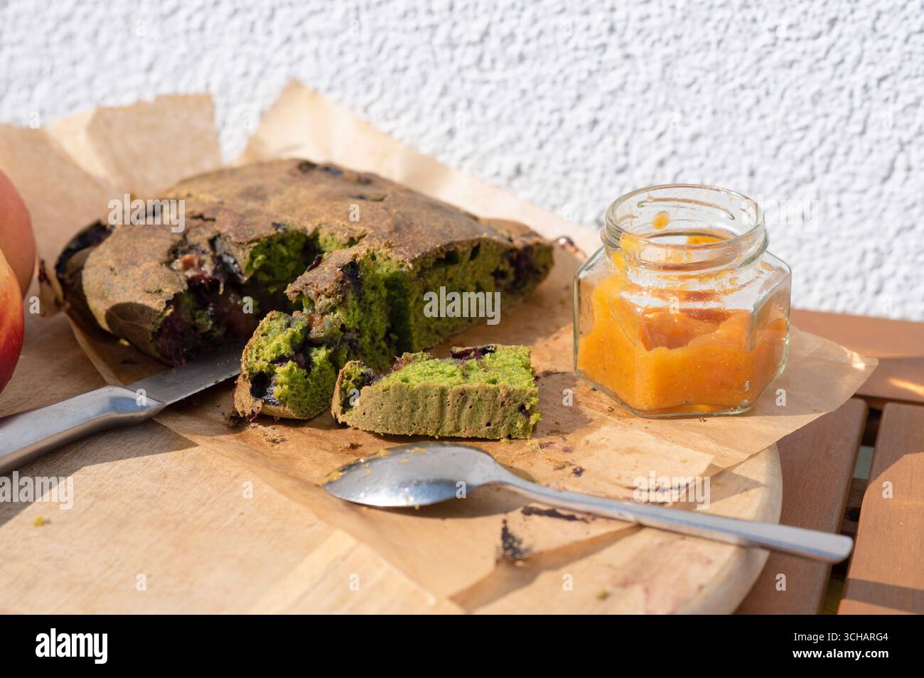 Rustikaler glutenfreier Spinatkuchen mit Pflaumen und hausgemachter Aprikosenmarmelade, mit Messer und Löffel auf einem Holzbrett. Gesunde hausgemachte Dessert Conceep Stockfoto