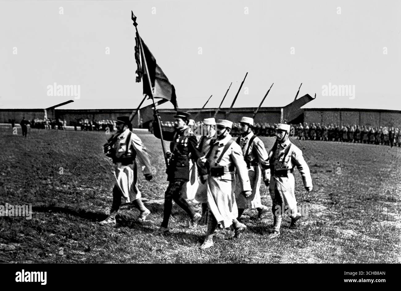 Sous-Leutnant Georges Guynemer, gefeiertes französisches Fliegerass des Ersten Weltkrieges, trug die Flugflagge als Fahnenträger. Dieses Schwarzweiß-Foto, das am 20. Mai 1916 in L’Illustration veröffentlicht wurde, zeigt Guynemer und seine Kollegen in Militärkleidung während einer zeremoniellen Parade mit Flugzeugen im Hintergrund. Guynemer wurde zum Nationalhelden für seine Luftsiege und symbolisierte Mut, Patriotismus und den Aufstieg der Luftfahrt in der modernen Kriegsführung. Stockfoto