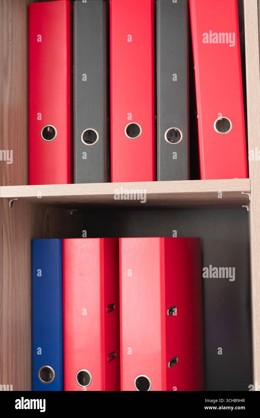 Eine farbenfrohe Sammlung von roten, schwarzen und blauen Büroordnern, die ordentlich in einem Regal angeordnet sind Stockfoto