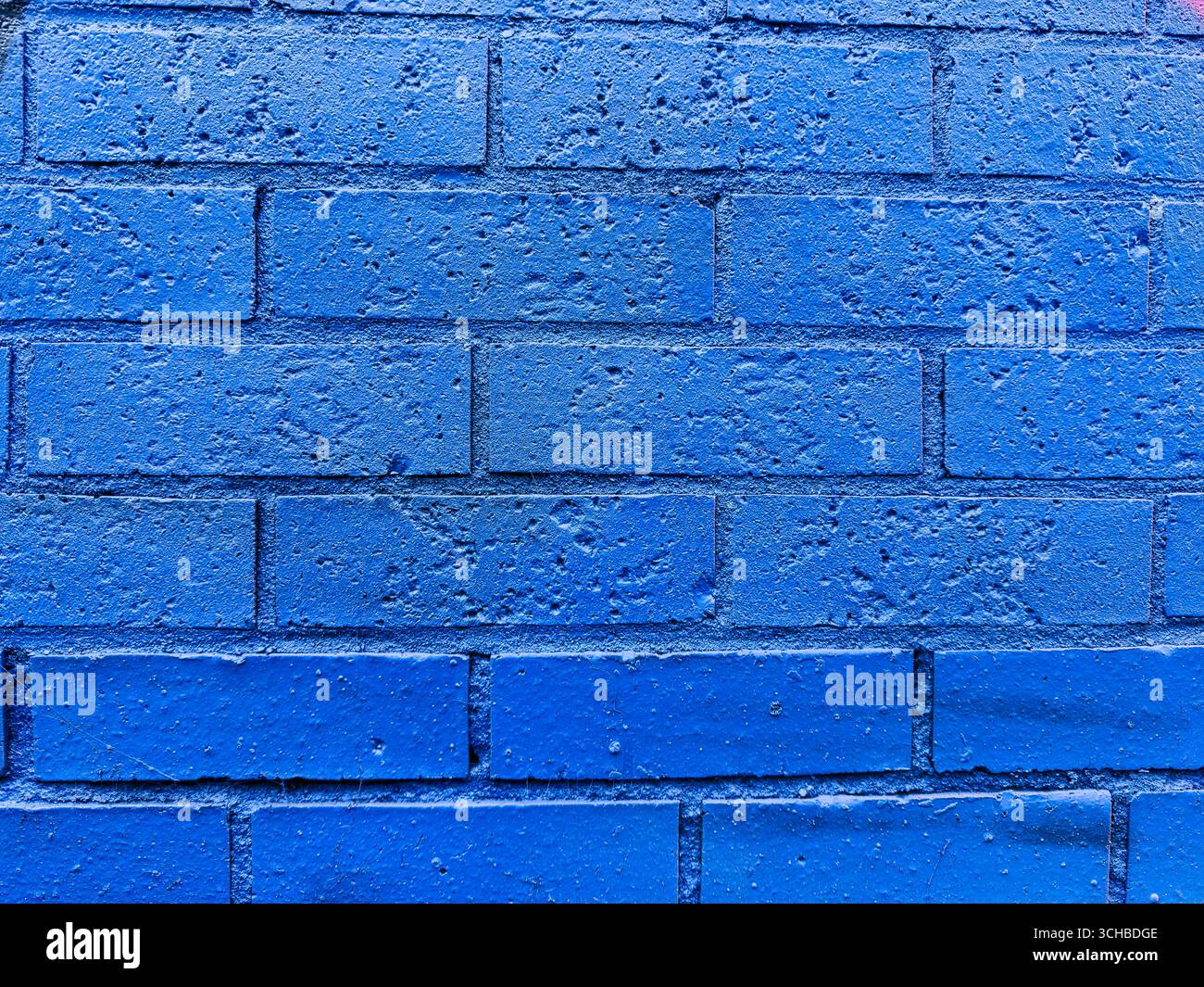 Nahaufnahme einer blau lackierten Ziegelwand mit sichtbarer Textur und Witterung, ideal für Hintergründe, Design oder architektonische Referenz. Stockfoto