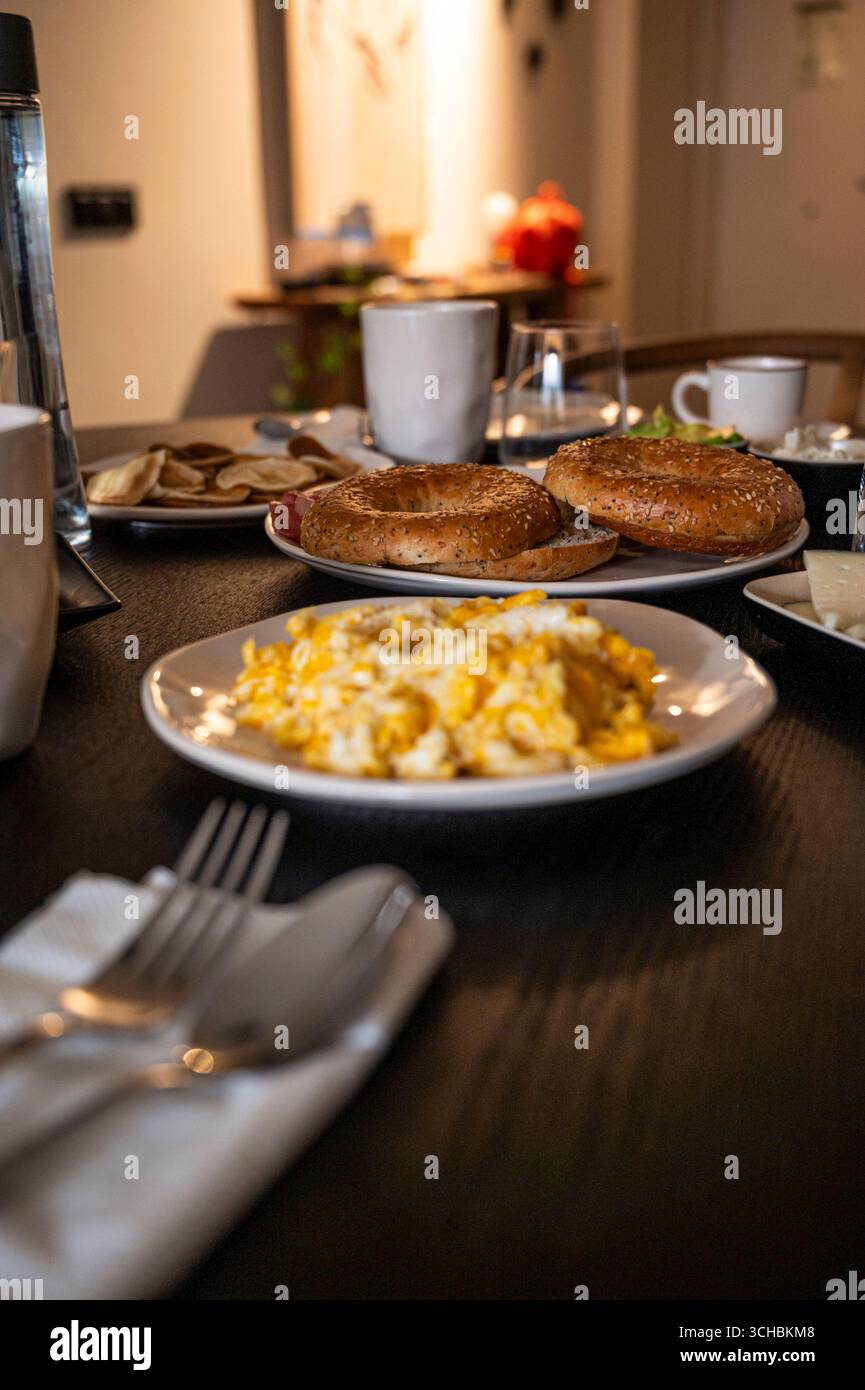 Ein Teller mit Eiern und Toast steht auf einem Tisch in einem schwach beleuchteten Raum. Der Tisch ist mit einer Vielzahl von Geschirr und Utensilien ausgestattet, darunter eine Gabel, ein Messer und ein Sp Stockfoto