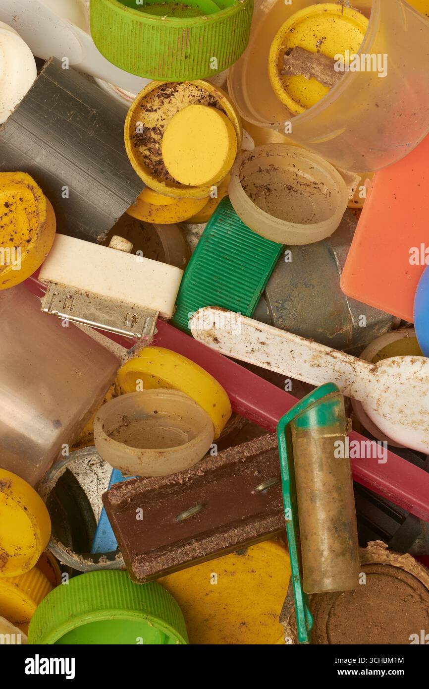 Stapel von verschmutzten, verwitterten Kunststoffabfällen, einschließlich Flaschenverschlüssen, Spielzeugteilen, Zahnbürste und Fragmenten im Vollformathintergrund, Umweltverschmutzung Stockfoto