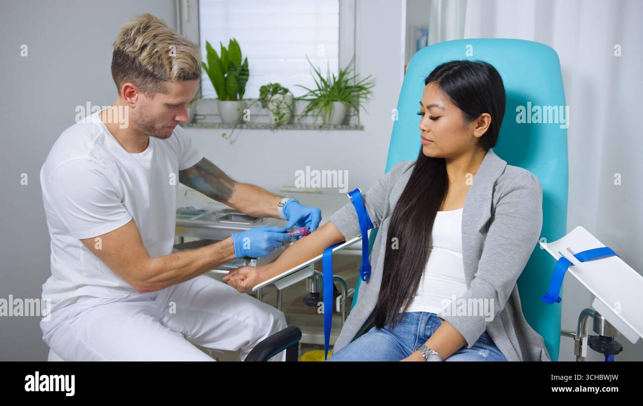 Eine Frau sitzt, während ein Arzt sie auf eine Blutspende in einer hellen Klinik vorbereitet. Stockfoto
