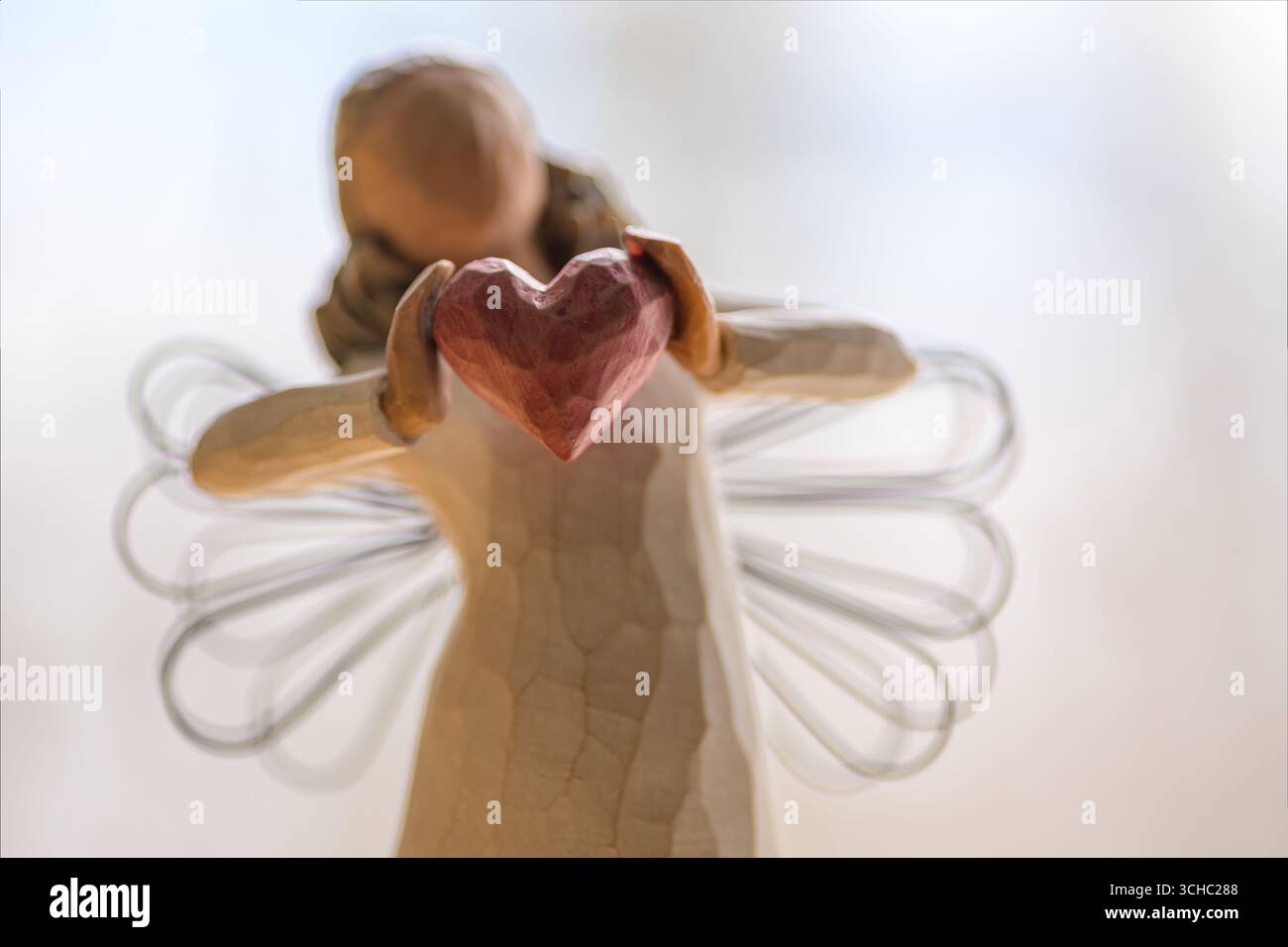 Eine hölzerne Engelsfigur hält ein Herz und symbolisiert Liebe, Mitgefühl und Sorgfalt. Stockfoto