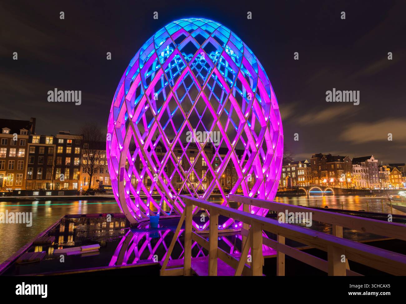 Amsterdams Innenstadt während des Amsterdam Light Festivals mit farbwechselnden Kunstwerken OVO, Künstler Koert Vermeulen, entlang des Flusses Amstel bei Nacht. Stockfoto