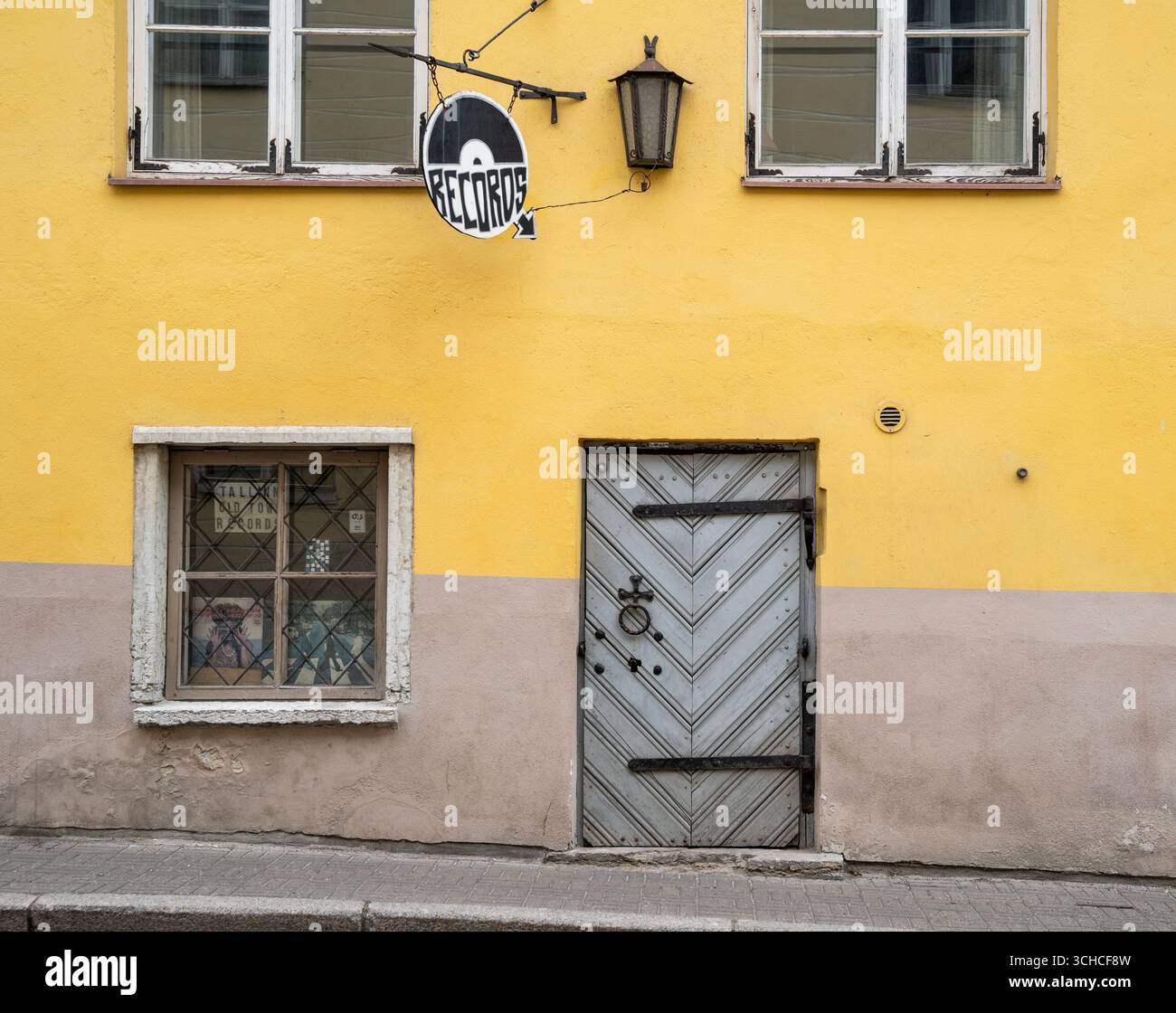 Farbenfrohe gelbe und rosafarbene historische Gebäudefassade mit Vintage-Holztür und Plattenschild in der Altstadt von Tallinn Stockfoto