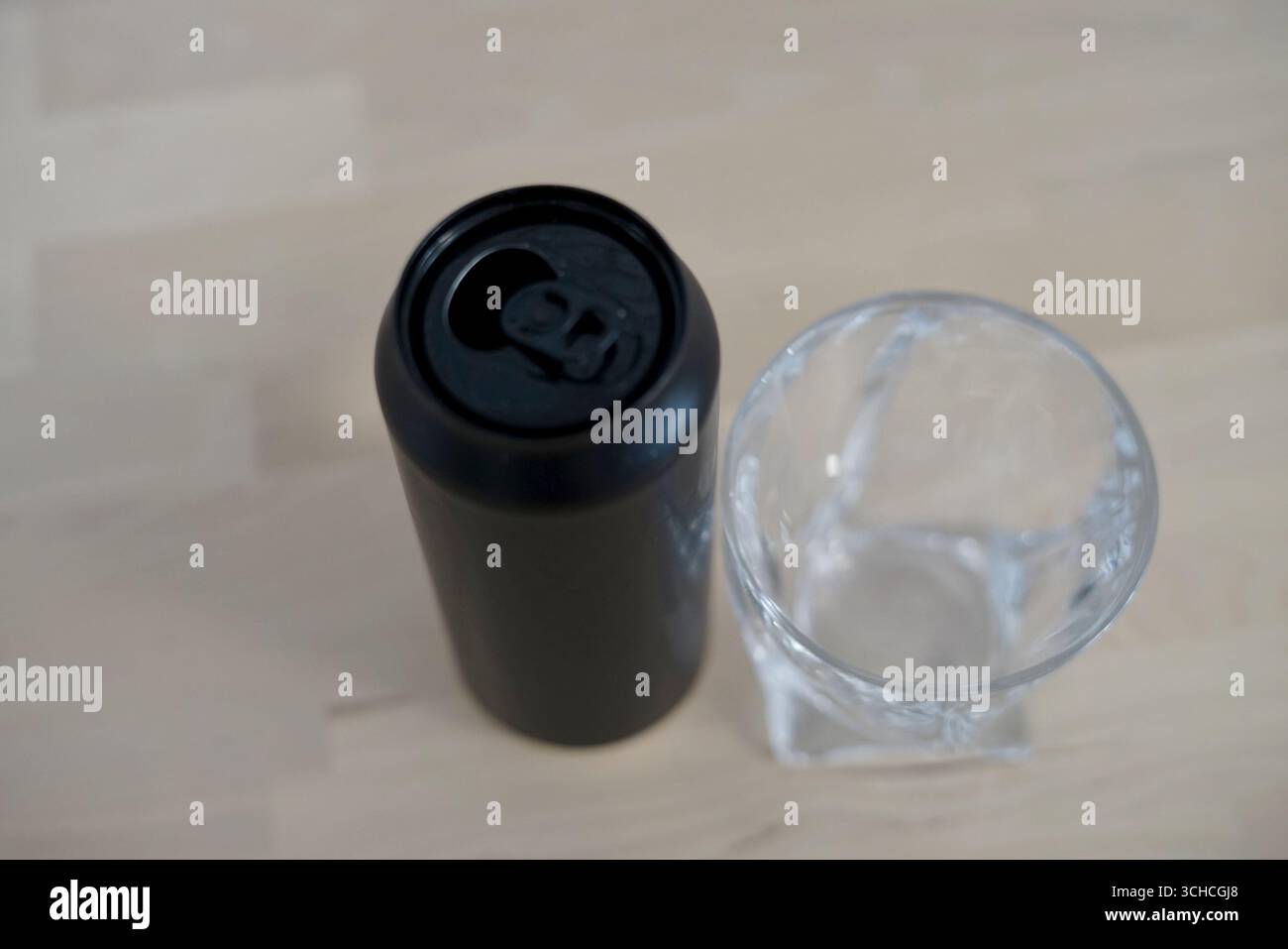 Eine schwarze Dose mit Schädeldesign und klarem Glas auf einer hellen Holzoberfläche, die die moderne Ästhetik des Getränks unterstreicht. Stockfoto