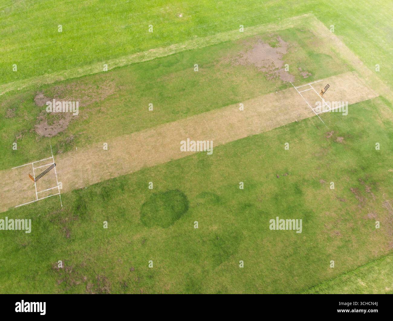 Zentraler Cricketplatz, der über das Grasfeld verläuft, mit Holzstümpfen und weißen Falten. Sport, Outdoor, Gelände, Freizeit, Spiel, Fitnes Stockfoto