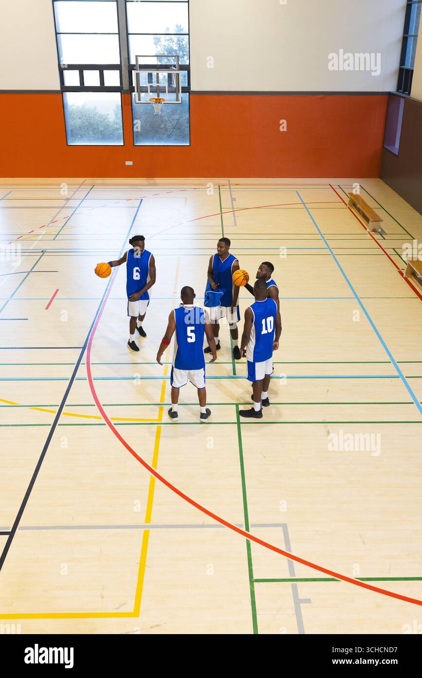Afroamerikanische Basketballmannschaft in blauen Trikots, die auf dem Platz mit orangen Basketbälle trainiert. Athleten, Teamwork, Sportlichkeit, Fitness, Training Stockfoto