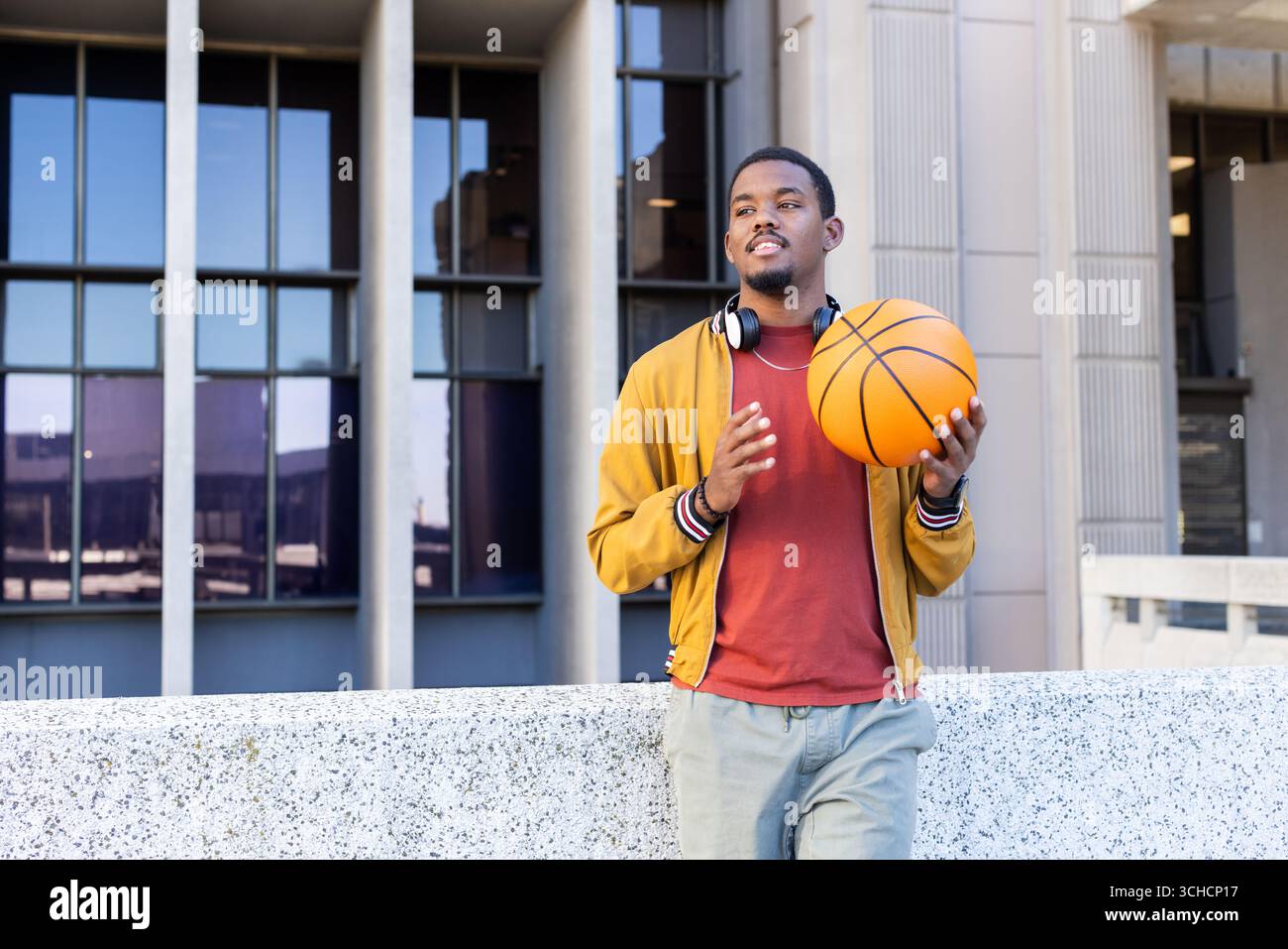 Afroamerikanischer Mann lehnt sich draußen mit Basketball und Kopfhörern an die Wand, Kopierraum. Urban, jugendlich, lässig, lebhaft, energiegeladen, modern, R. Stockfoto