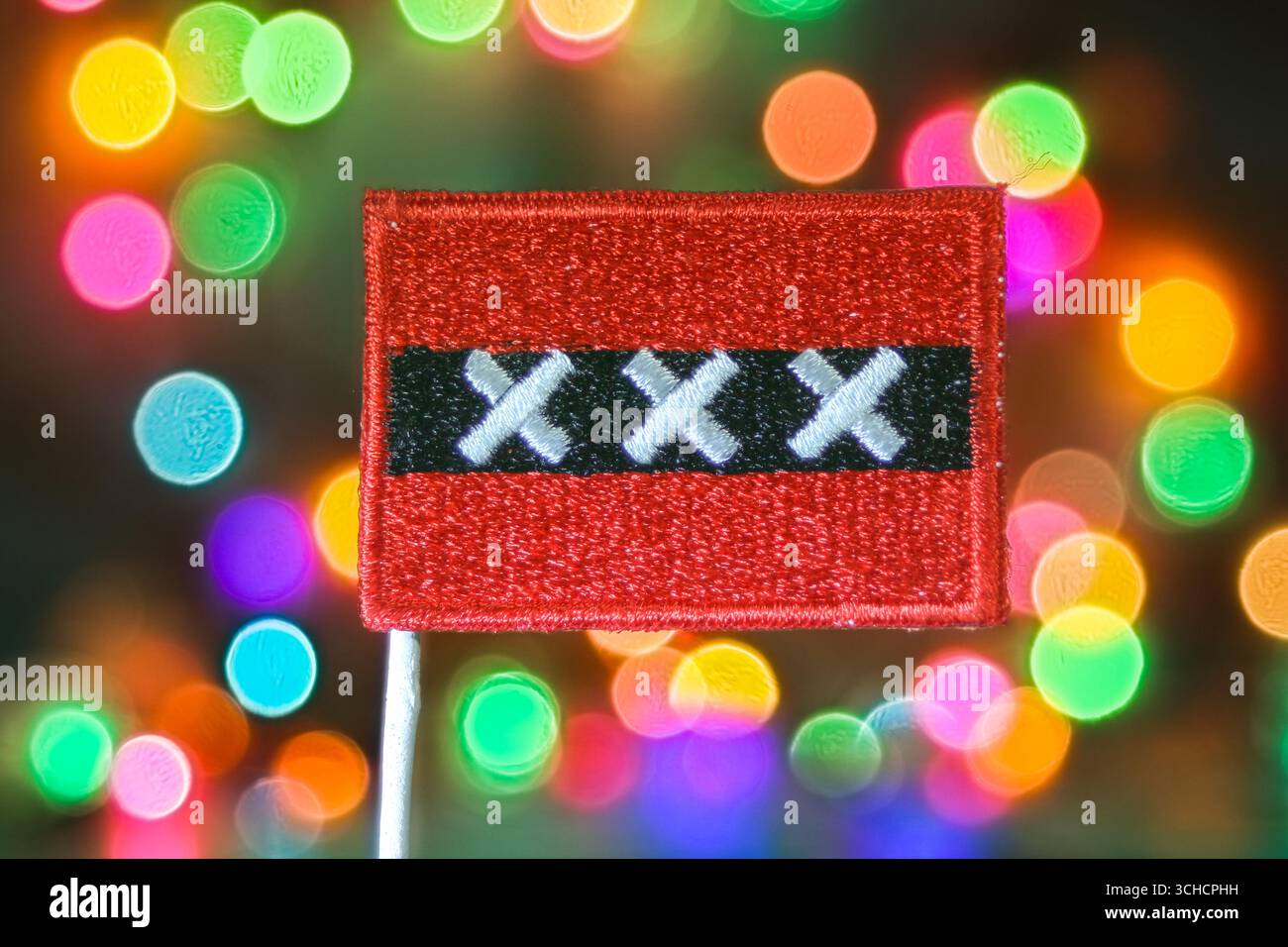 Gestickte Amsterdamer Flagge mit mehrfarbigem Bokeh-Licht-Hintergrund, festliches Stadtfest mit europäischer Kultur und Feststimmung. Stockfoto