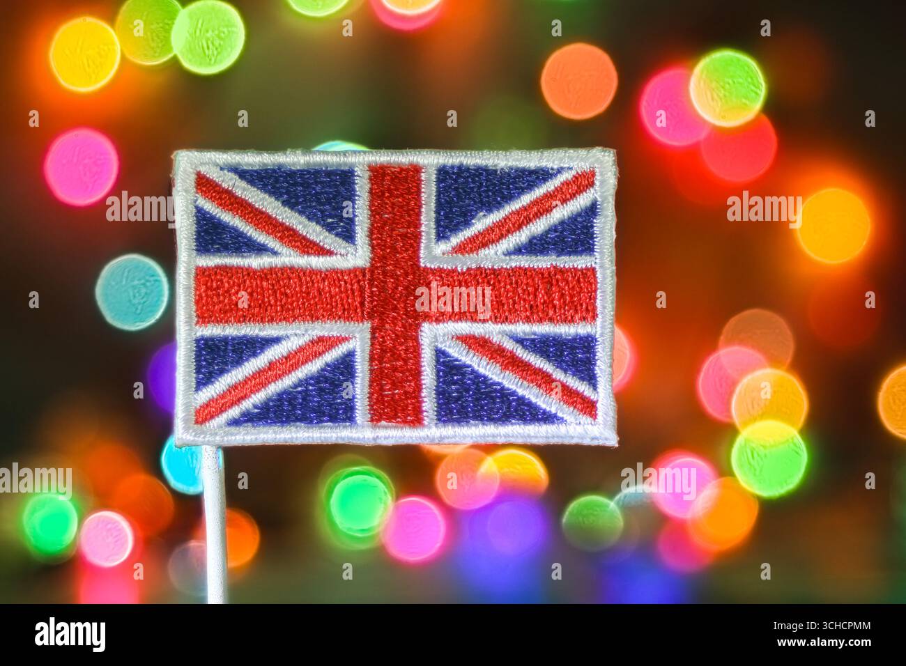 Die Stickerei der Union Jack-Flagge vor farbenfrohen Bokeh-Lichtern symbolisiert den Stolz Großbritanniens, die Feiertage und festliche Veranstaltungen. Stockfoto