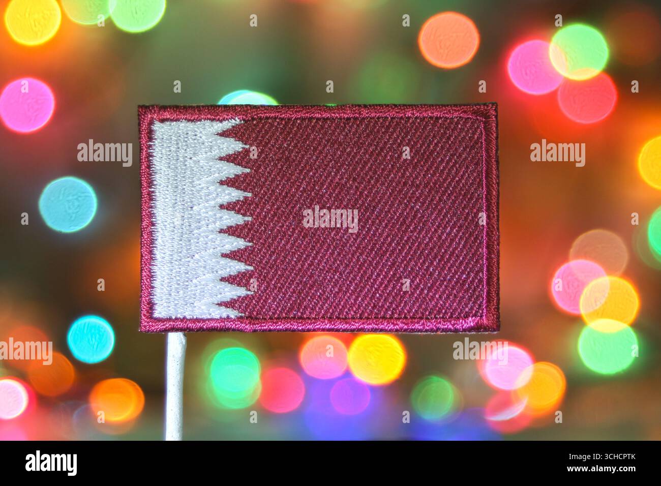 Die Stickerei mit der katarischen Nationalflagge mit festlichen Regenbogenbokeh-Lichtern symbolisiert Feuerwerk und Neujahrsfeiern in Doha. Stockfoto