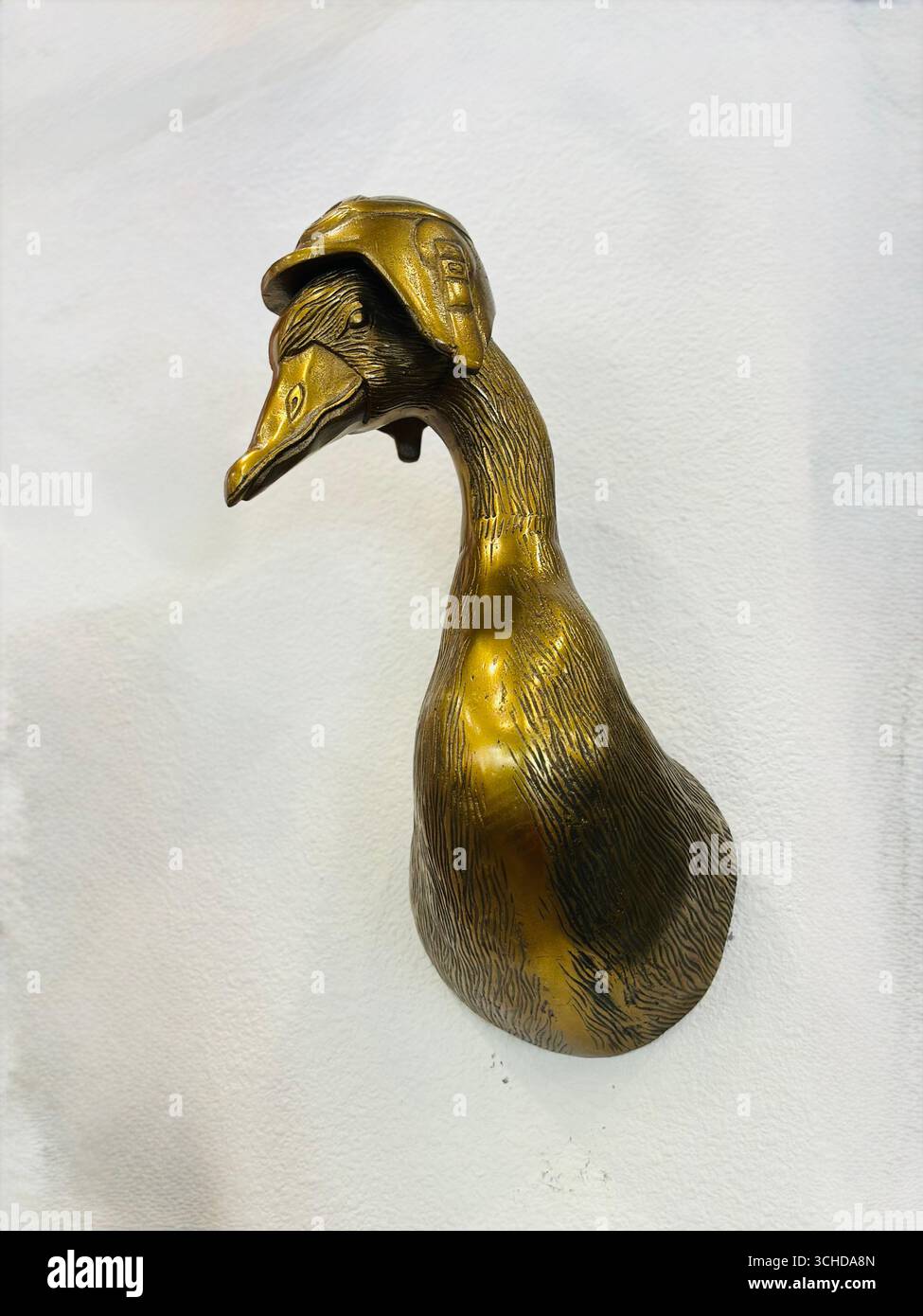 Eine dekorative Bronze-Entenkopf-Skulptur im Vintage-Stil mit Pilotenhelm, isoliert auf weißem Hintergrund. - Smartphone-aufgenommenes Stockfoto