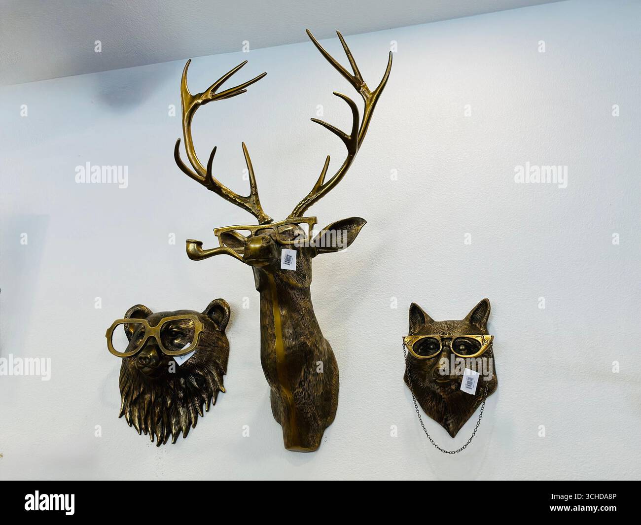 Skulpturen aus Bronze mit Tiermalereien, darunter ein Bär, ein Hirsch und ein Wolf, die jeweils mit einer Brille verziert sind und auf einer weißen Wand ausgestellt sind. Stockfoto