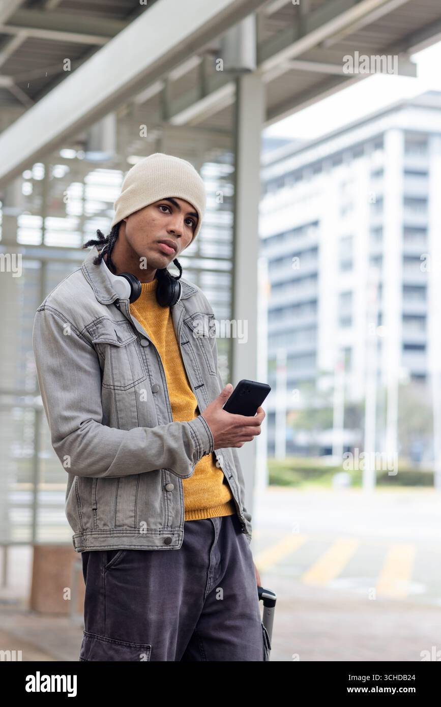 Junger Mann, der im Transitunterstand steht und ein Smartphone und einen Reisebecher aus Edelstahl hält Stockfoto