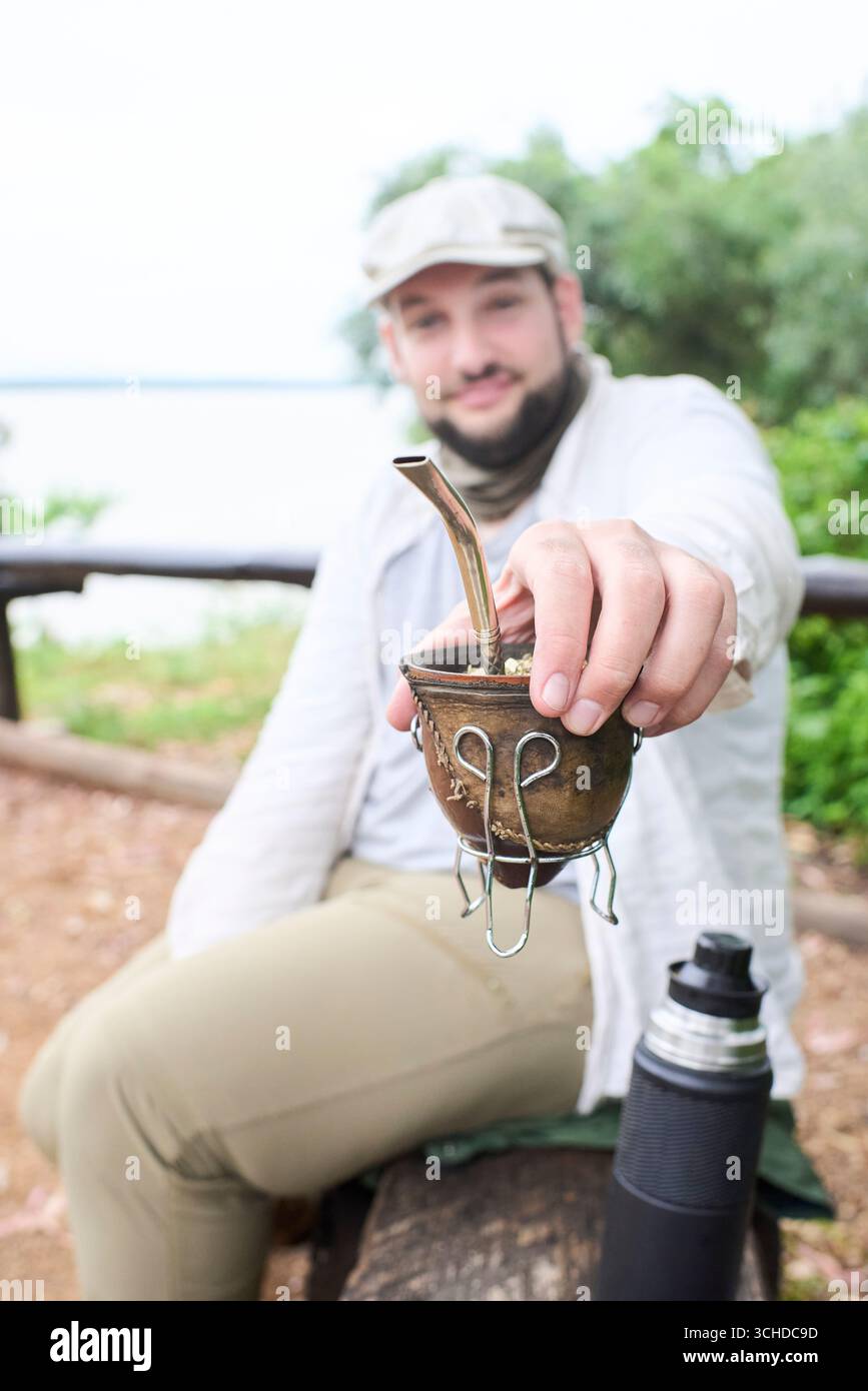 Ein lächelnder Mann bietet der Kamera einen Kameraden an. Dieses argentinische Getränk ist ein Symbol für das Teilen und Zusammensein. Komposition mit selektivem Fokus auf den han Stockfoto