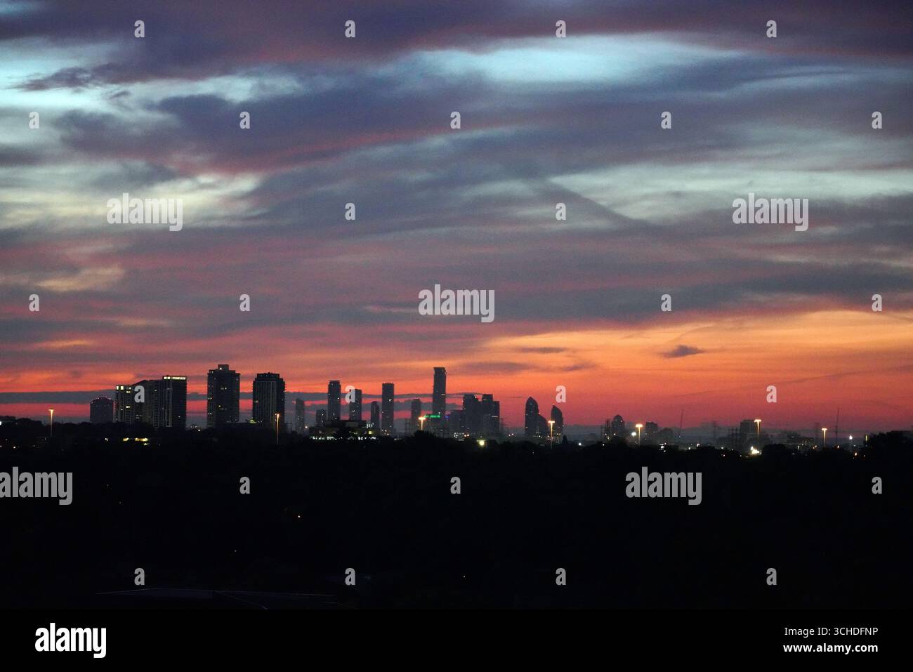 Der leuchtende Sonnenaufgang überzieht den Himmel in Rot-, Orange- und Violetttönen über einer Silhouette der Stadt Stockfoto