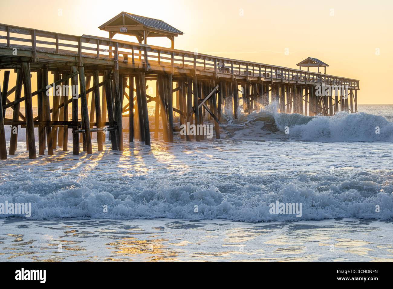 Sonnenaufgang am Amelia by the Sea Ocean Pier in Fernandina Beach, Florida, auf Amelia Island, während die Wellen eindringen und gegen die Pier-Anhäufungen krachen. (USA) Stockfoto