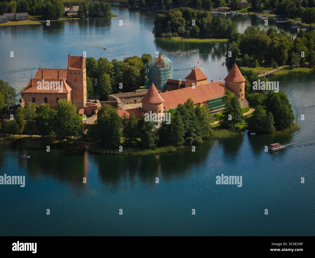 Blick aus der Vogelperspektive auf die mittelalterliche Burg Trakai, eine markante Festung aus rotem Backstein, die sich im glitzernden Wasser des Galvė-Sees spiegelt, umgeben von grünen Wäldern, Trakai, Litauen. Stockfoto