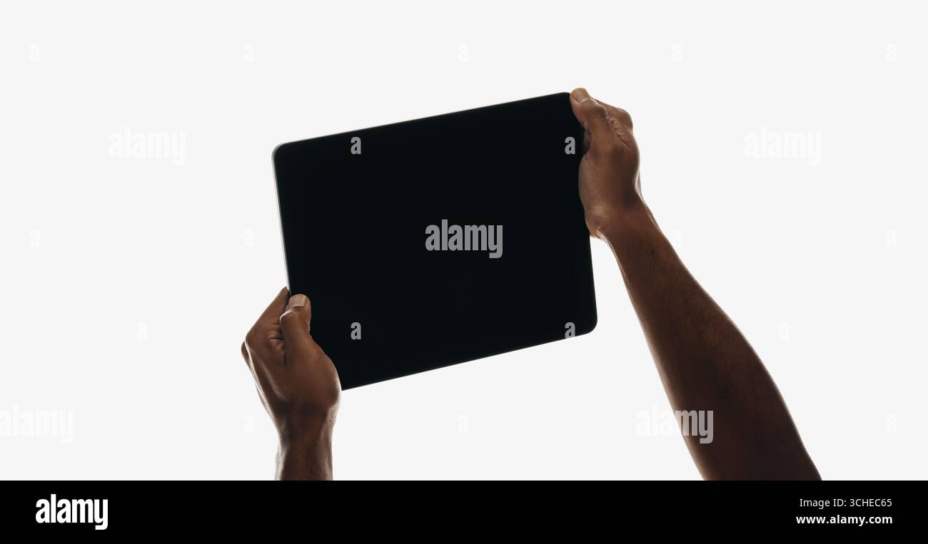 Ein Paar Hände heben ein schwarzes Tablet-Gerät vor einem schlichten weißen Hintergrund und betonen so Technologie und moderne Designelemente. Stockfoto