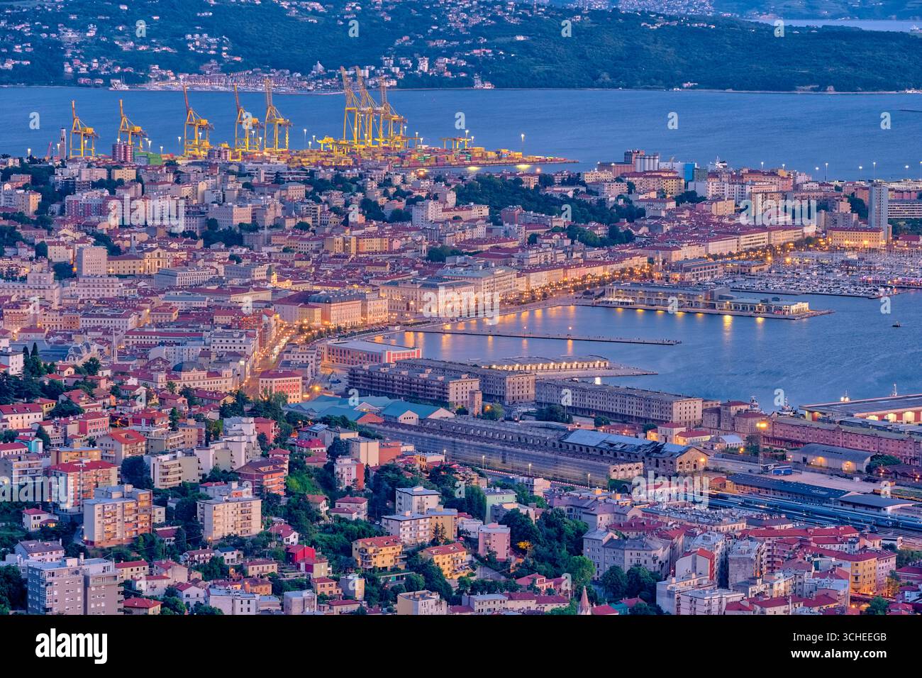 Aus der Vogelperspektive auf die Häuser, den Yachthafen und die Kräne des Überseehafens von Triest, beleuchtet bei Nacht. Triest Friaul-Julisch Venetien Italien FB 20 Stockfoto