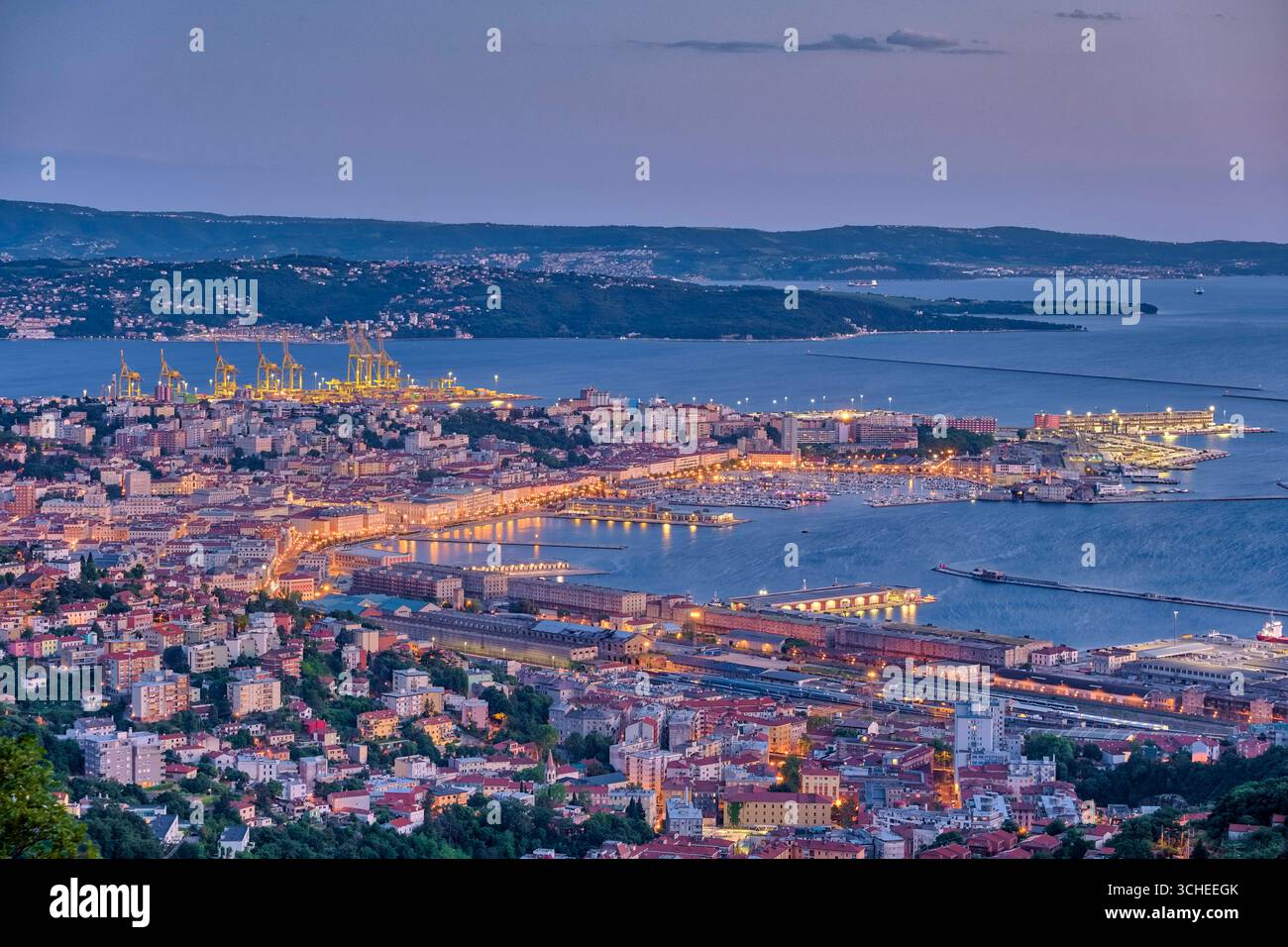 Aus der Vogelperspektive auf die Häuser, den Yachthafen und die Kräne des Überseehafens von Triest, beleuchtet bei Nacht. Triest Friaul-Julisch Venetien Italien FB 20 Stockfoto