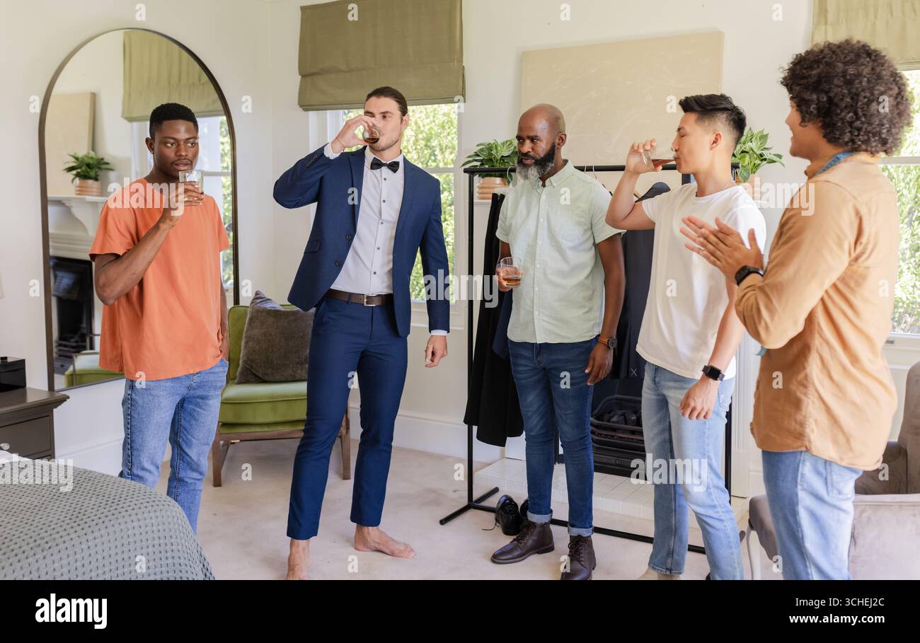Hochzeitsanzüge, feiert männliche Freunde, die im Schlafzimmer klatschen und Drinks trinken, mit klaren Gläsern Stockfoto