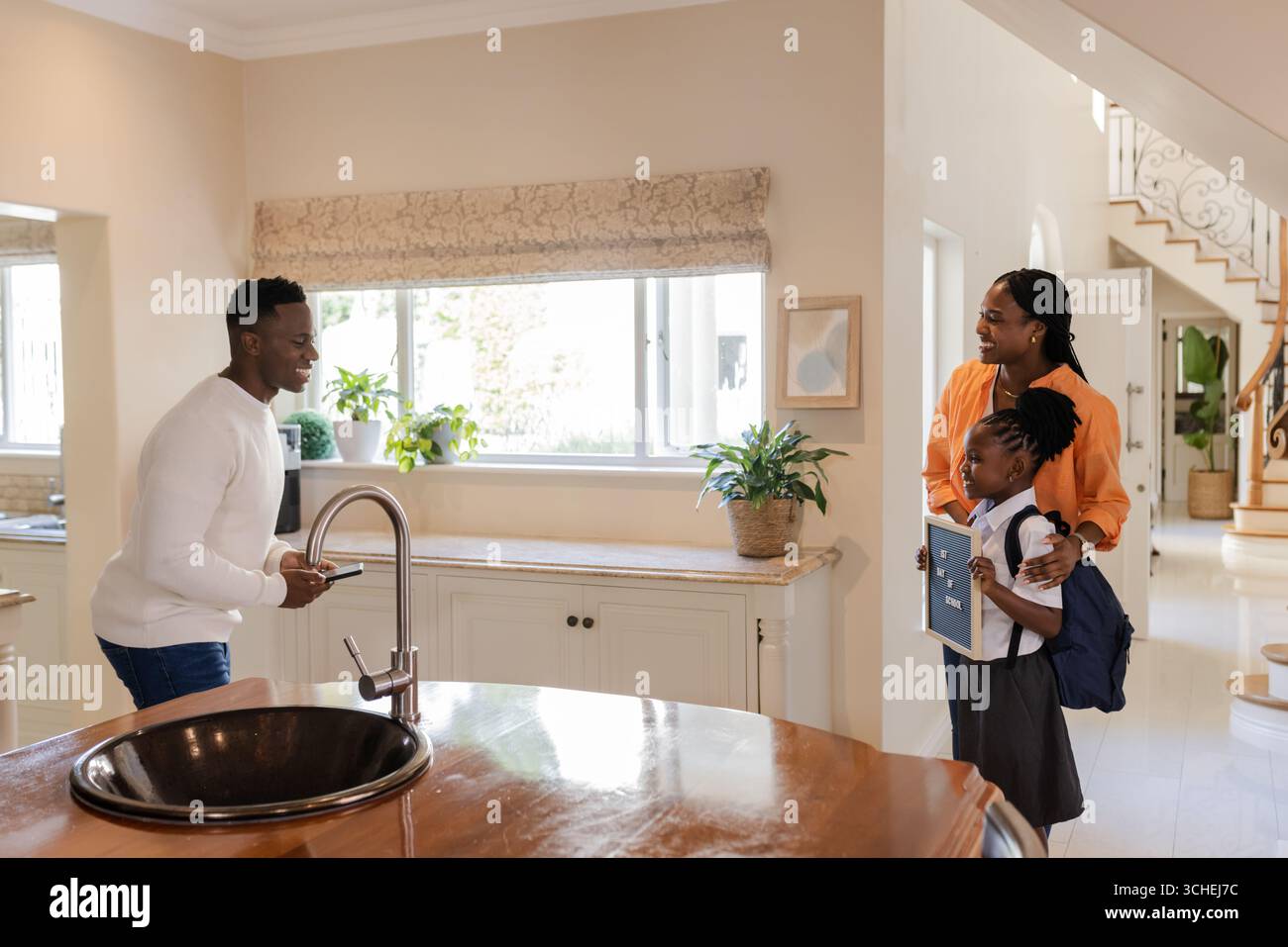Vater grüßt Tochter und Mutter zu Hause, Tochter mit Schulrucksack Stockfoto