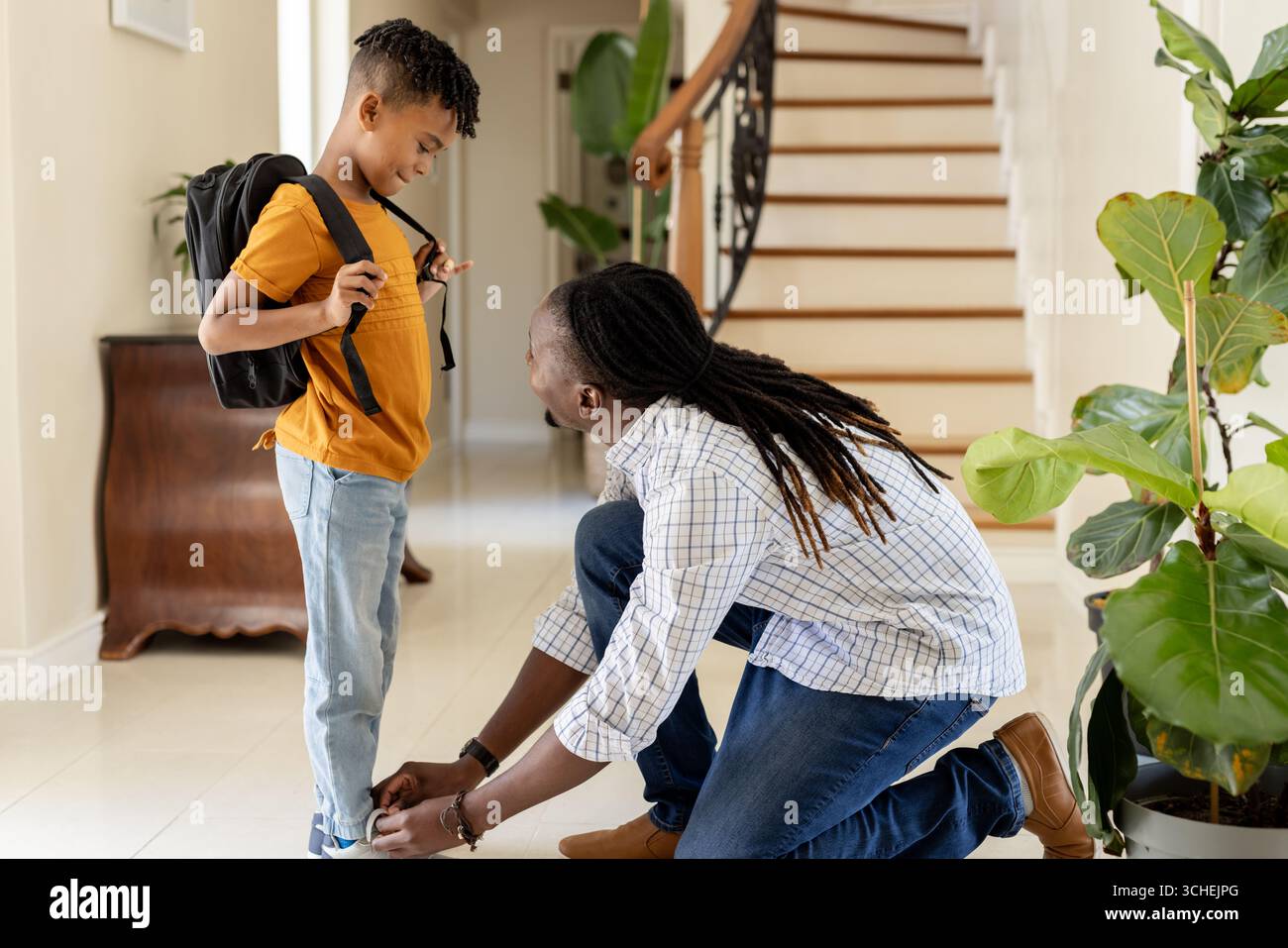 Der afroamerikanische Vater bindet zu Hause die Schuhe des Sohnes und bereitet sich auf die Schule vor Stockfoto