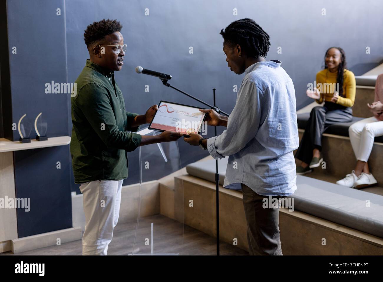 Im Büro, auf der Bühne präsentieren zwei Männer den Preis, während das Publikum begeistert applaudiert Stockfoto