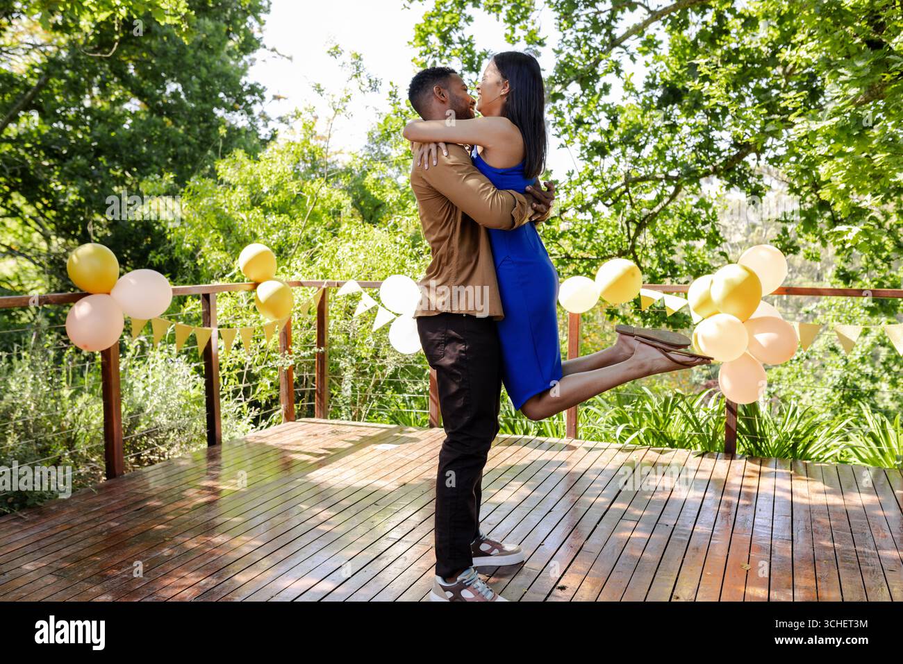 Ein Paar feiert die Verlobung an Deck, ein Mann hebt eine Frau, umgeben von Ballonen Stockfoto