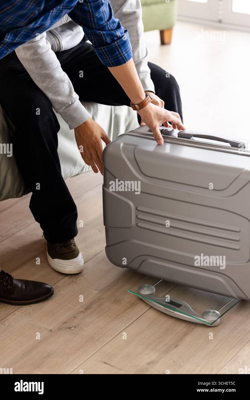 Vater und Sohn wiegen den Koffer zu Hause auf einer digitalen Waage, bereiten sich auf die Reise vor Stockfoto