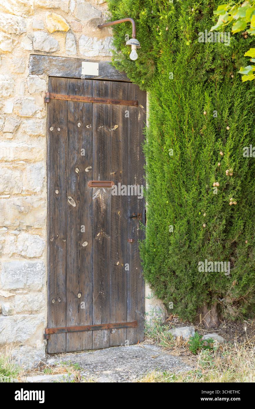 Verwitterte Holztür mit rostigen Scharnieren und grüner Hecke in einem mittelalterlichen Dorf in Drome, Frankreich Stockfoto