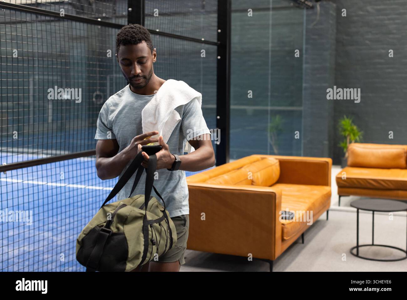 afroamerikanischer Mann mit Handtuch, der das Smartphone in der Padel-Lounge überprüft Stockfoto