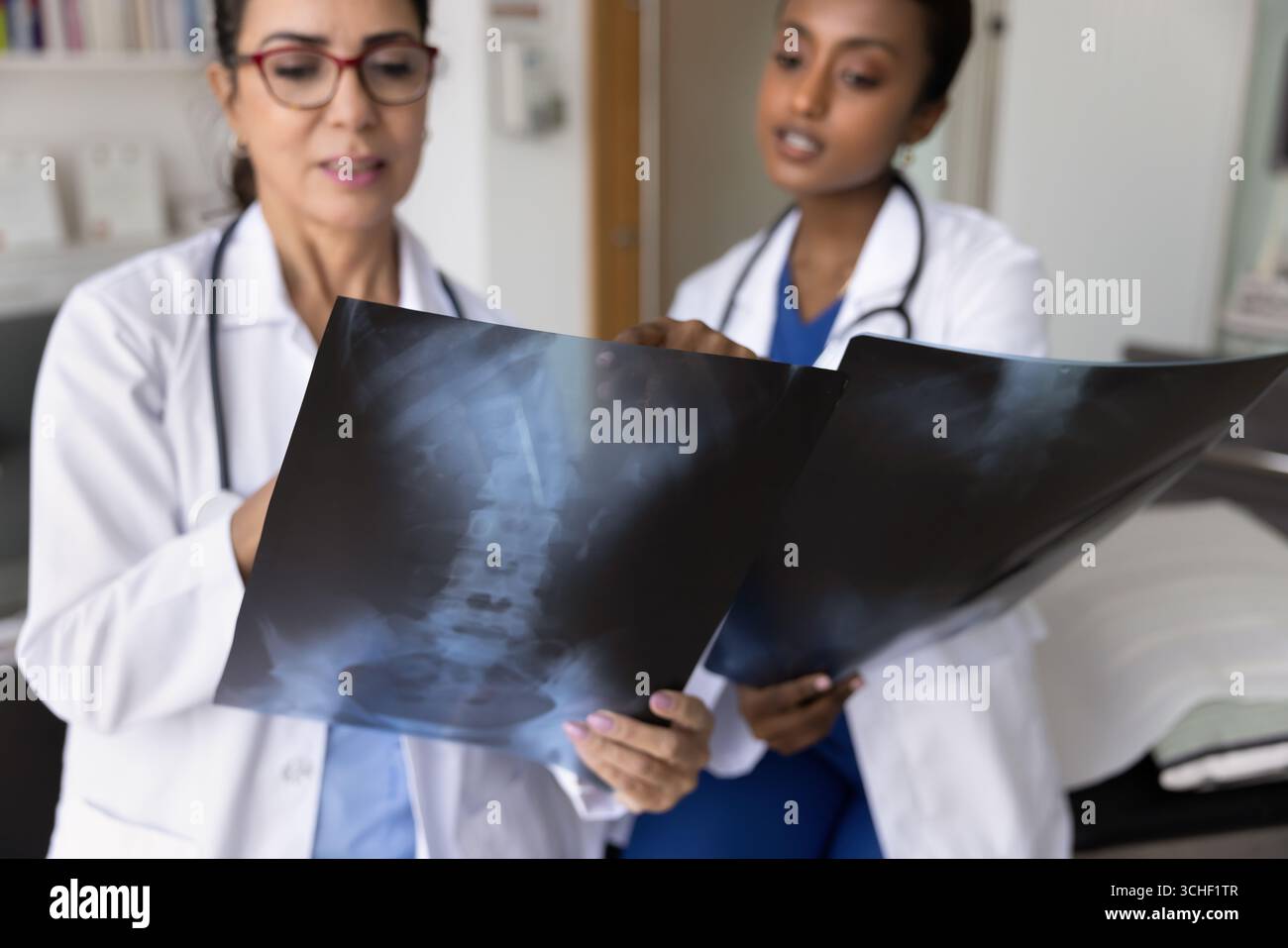 Zwei jüngere und ältere Ärztinnen, die Röntgenbilder überprüfen Stockfoto