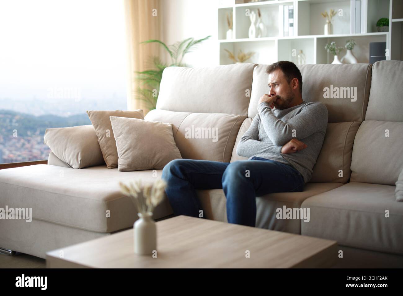 Trauriger Mann, der sich allein beschwert und zu Hause oder im Hotelzimmer durch ein Fenster schaute Stockfoto