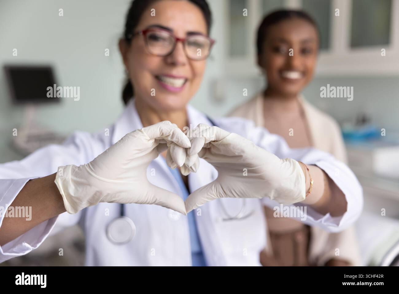 Arzt zeigt Herzsymbol mit Händen, glücklicher Patient im Hintergrund Stockfoto